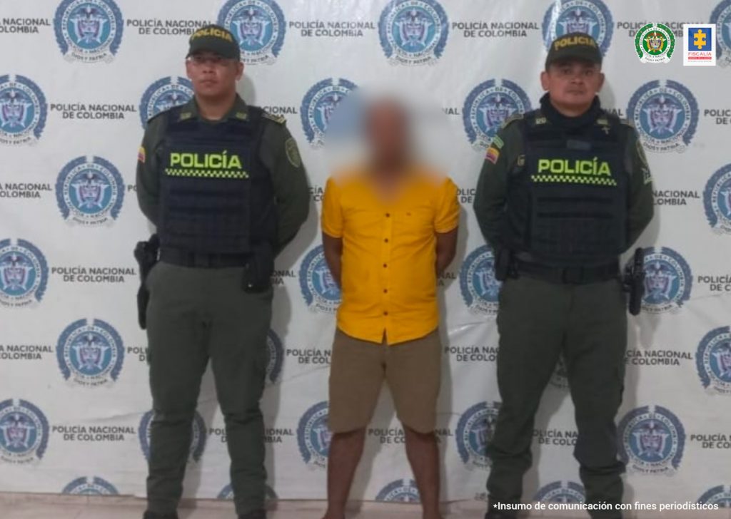 En la fotografía aparece un hombre capturado, acompañado de dos uniformados de la Policía. En la parte posterior un banner con logos de la entidad.