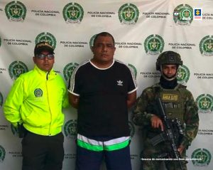 En la imagen se ve una persona de suéter negro entre dos uniformados. 