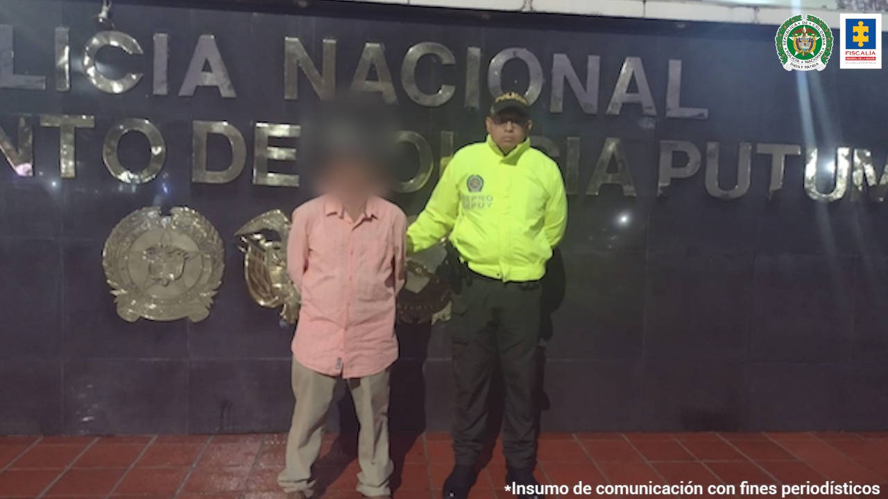 En la fotografía aparece un capturado junto a personal de Policía Nacional. En la parte posterior de la imagen se ven banners de Policía y la Fiscalía General de la Nación.     