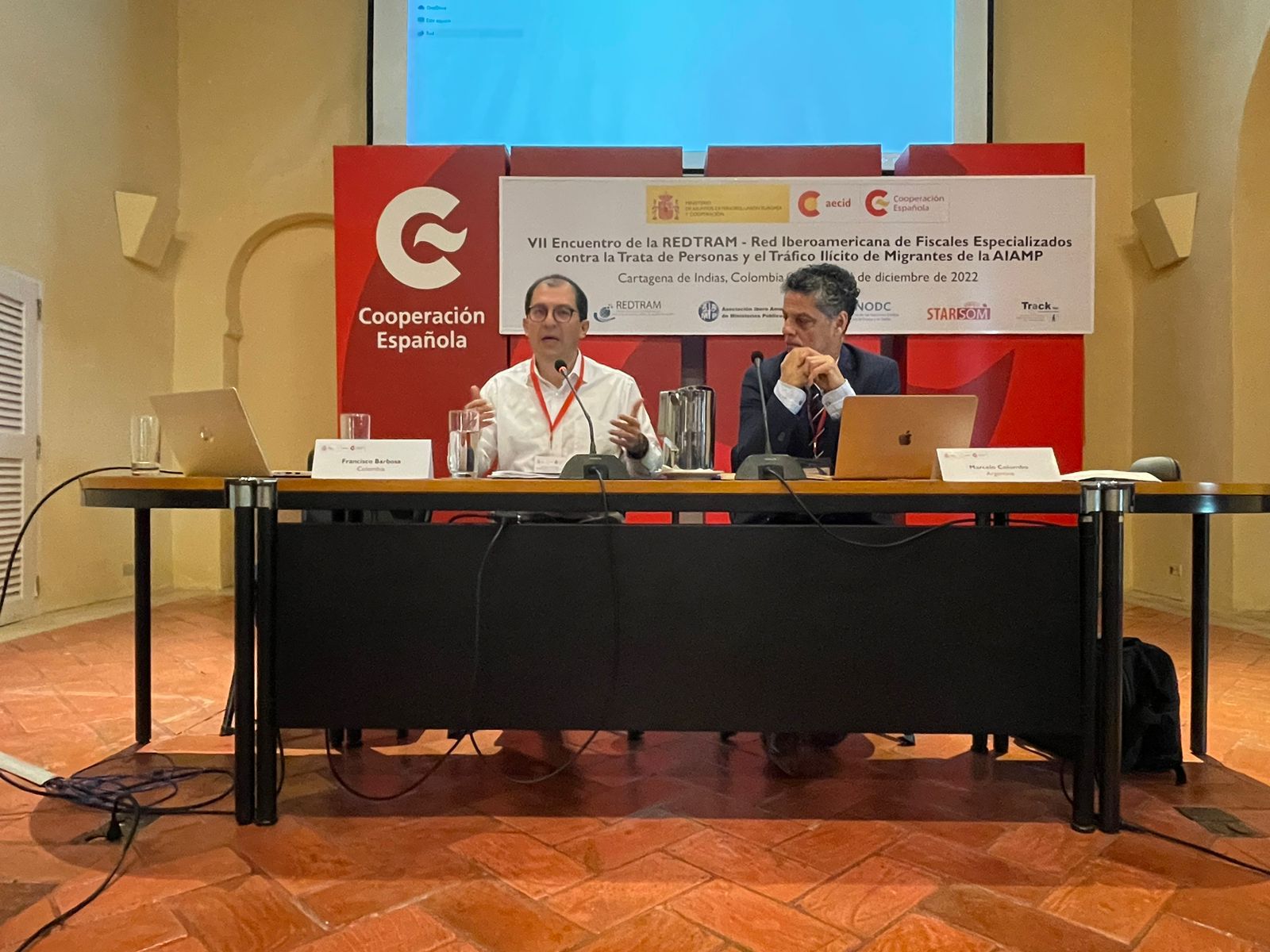 Fiscal General de la Nación durante una conferencia, sentado junto a otra persona.