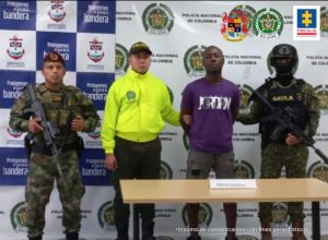 En la fotografía se observa al capturado junto a un agente de la Policía y a dos soldados del Gaula Militar. En la parte superior se observa un banner de la Policía Nacional y otro banner del Gaula Militar 