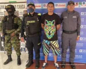 En la fotografía se observa al capturado junto a un servidor del CTI, un agente de la Policía Nacional y un soldado del Ejército Nacional. En la parte superior se observa un banner de la Policía Nacional 