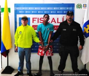 En la fotografía está el capturado junto a un servidor del CTI y un agente de la Policía Nacional. En la parte superior se observa un banner de la Fiscalía General