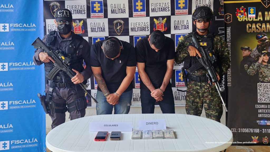 Los capturados aparecen con sus caras agachadas y custodiados por servidores del CTI de la Fiscalía y Gaula Ejército. En una mesa delante de ellos, están los celulares y el dinero incautado durante la captura.
