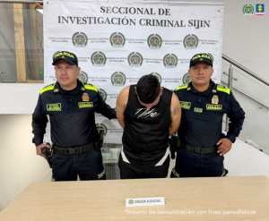 Se visualiza al capturado junto a dos uniformados de la Policía Nacional. Detrás de ellos el banner que identifica a la Policía Nacional.