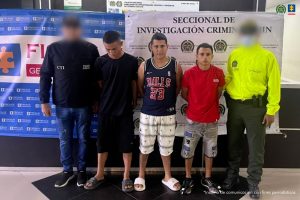 Se visualiza a los capturados junto a un investigador del CTI y uniformado de la Policía Nacional. Detrás se ubican los banners de la Fiscalía General de la Nación y de la Policía Nacional 