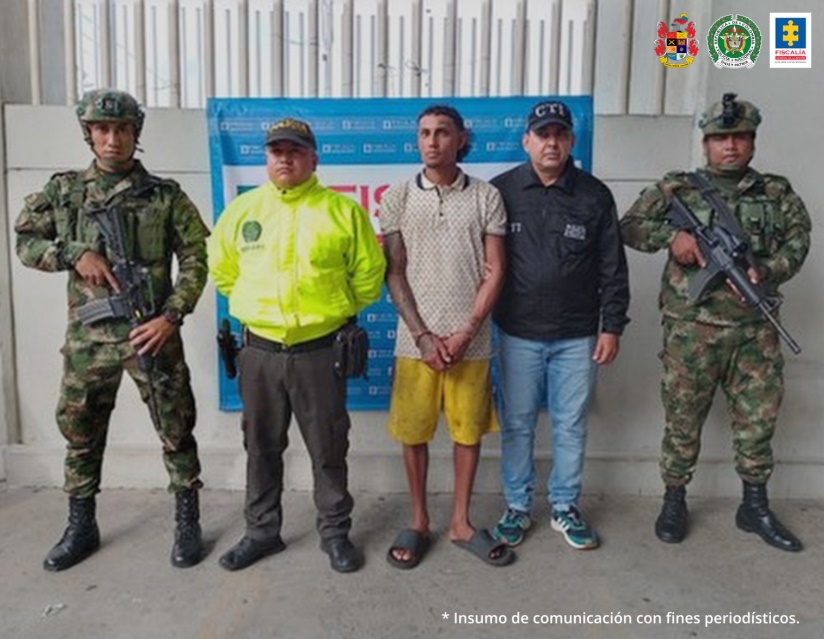 En la fotografía se observa a los dos capturados junto a un investigador del CTI y uniformados de la Policía y Ejército Nacional. En la parte posterior se aprecia el banner de la Fiscalía General de la Nación. 