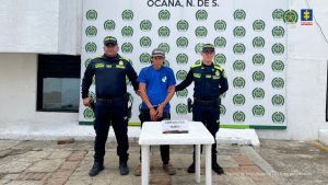 Se observa al capturado junto a dos uniformados de la Policía Nacional. Frente a ellos el arma cortopunzante utilizada para el hurto. Detrás el banner que identifica a la Policía Nacional en Ocaña.