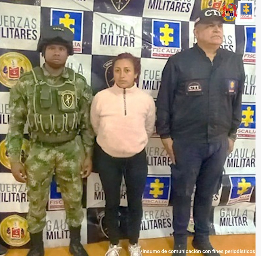 en la imagen se ve una mujer detenida bajo custodia de un investigador del CTI y del Gaula Militar. Detrás suyo un backing institucional.