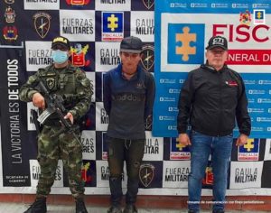 en la imagen se ve una persona detenida bajo custodia de un investigador del CTI y un integrante del Ejército Nacional. Detrás suyo backings institucionales.