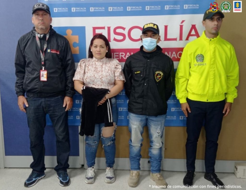 En la imagen se ve una mujer detenida bajo custodia de investigadores del CTI, Policía y Ejército. Detrás suyo un backing de la Fiscalía. 